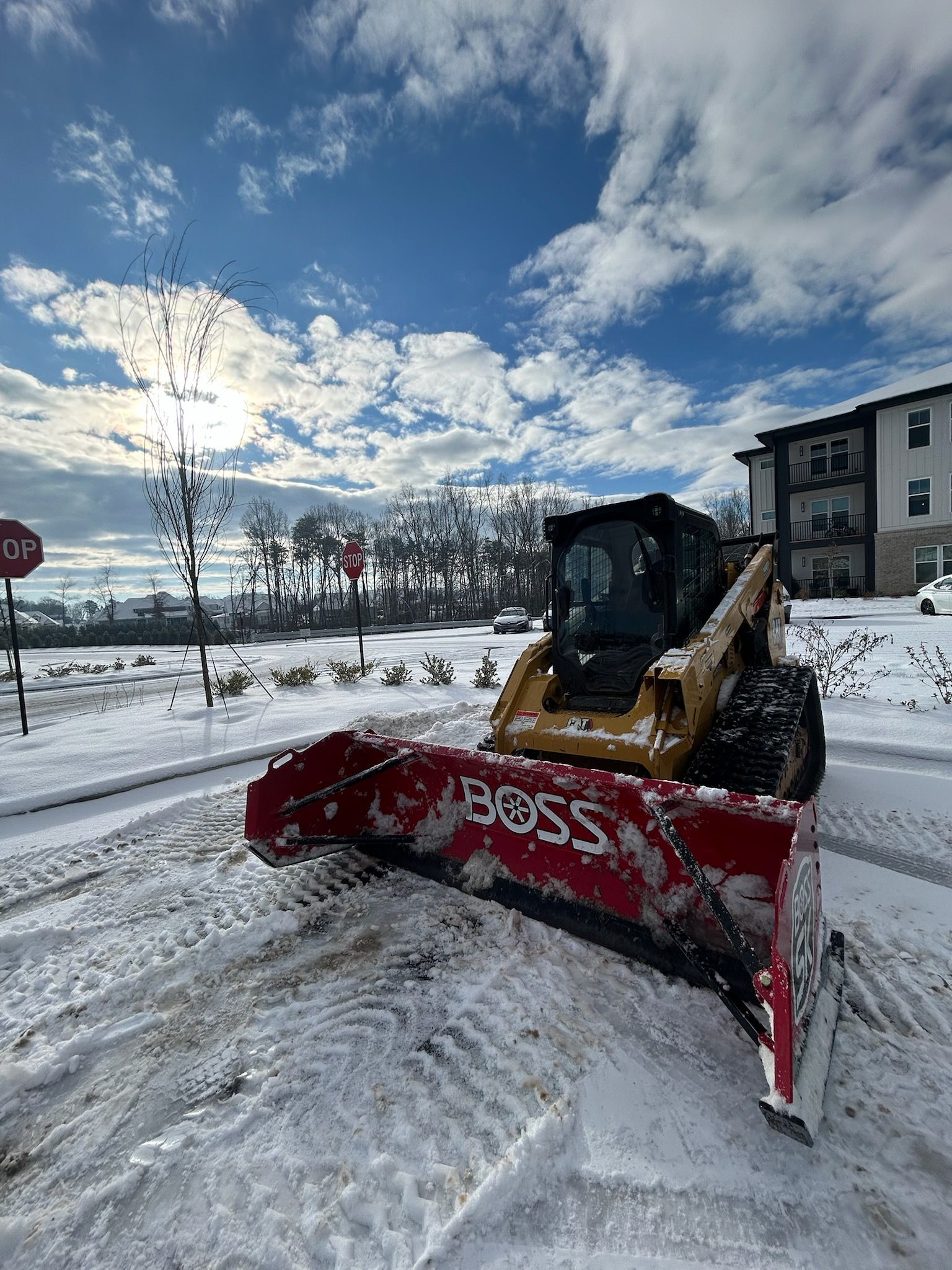 Snowplow clearing a snowy road under a bright blue, partly cloudy sky
