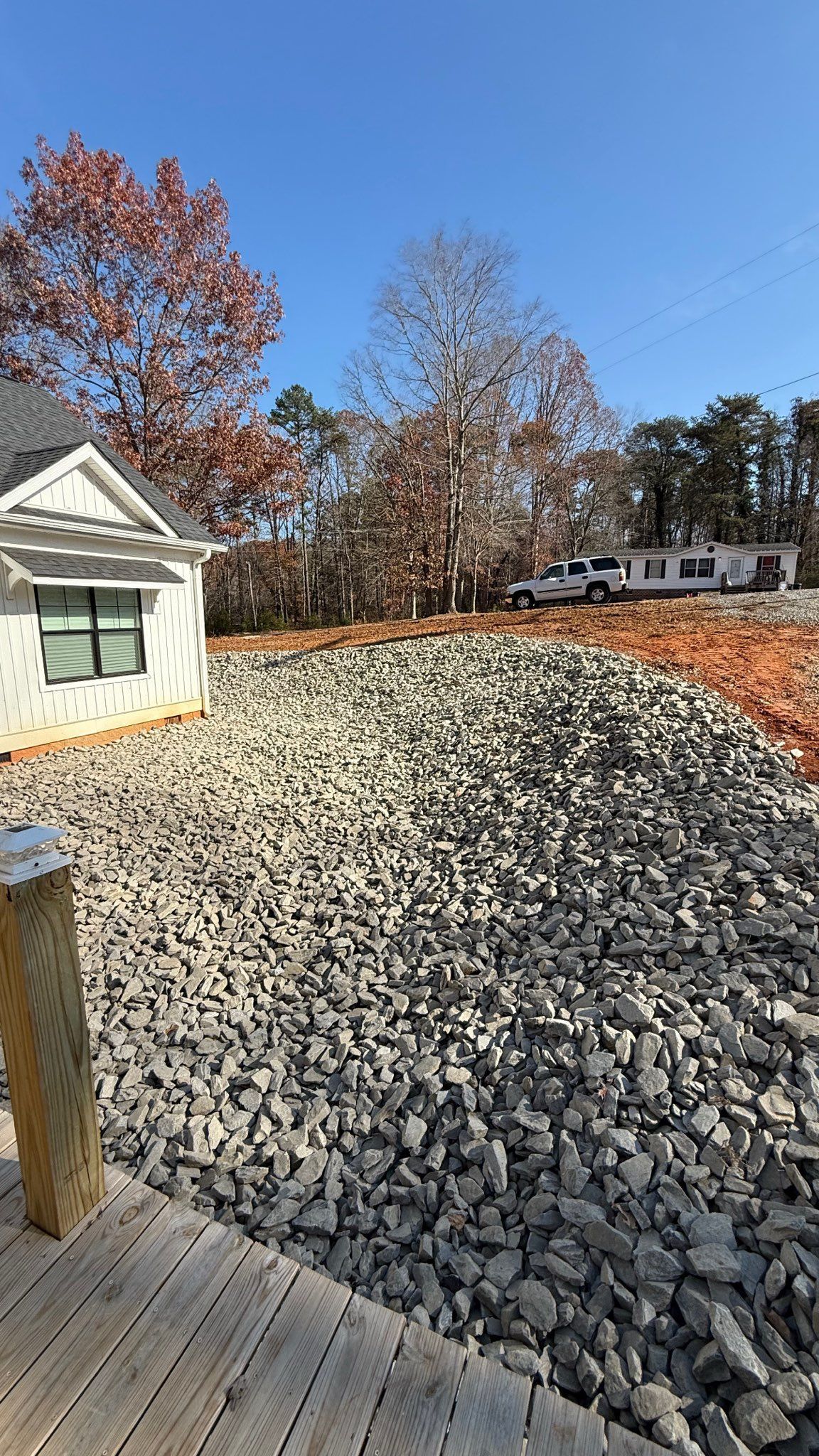 Gravel-covered lot beside a white house, with autumn trees and a wooden deck in the foreground
