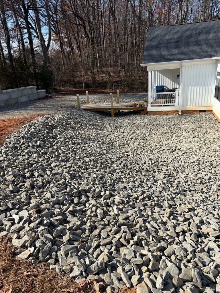 Gravel-covered yard beside a small white shed and raised deck, with bare trees in the background