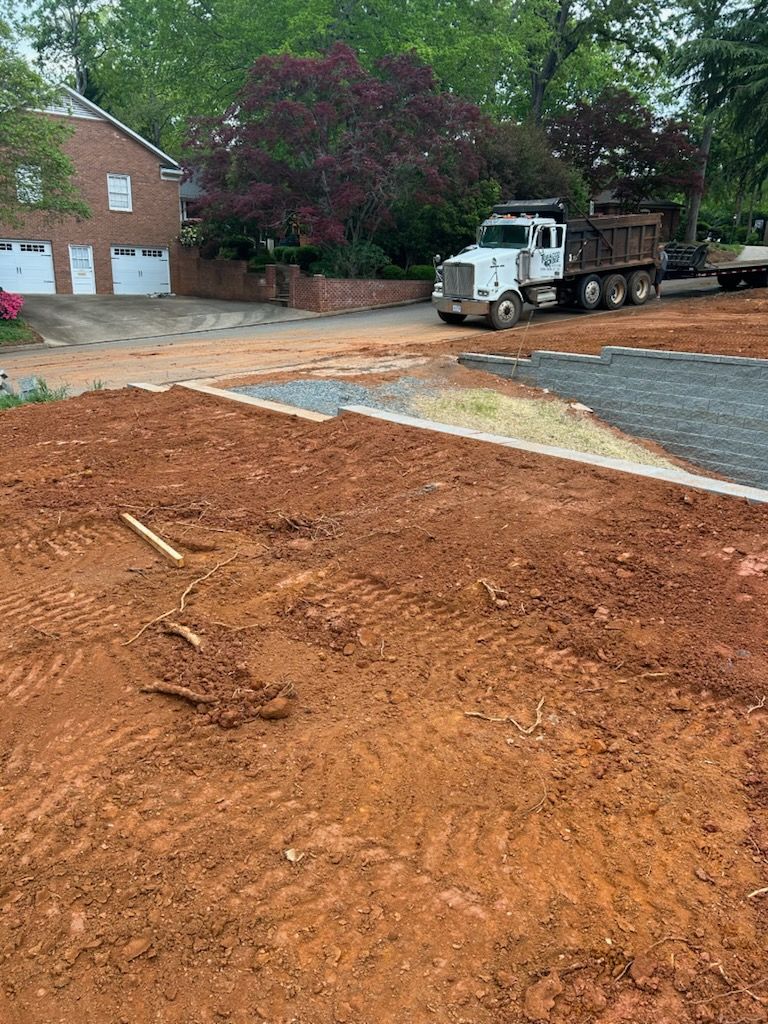 Construction site with dirt foreground, brick house, and white truck parked near trees.