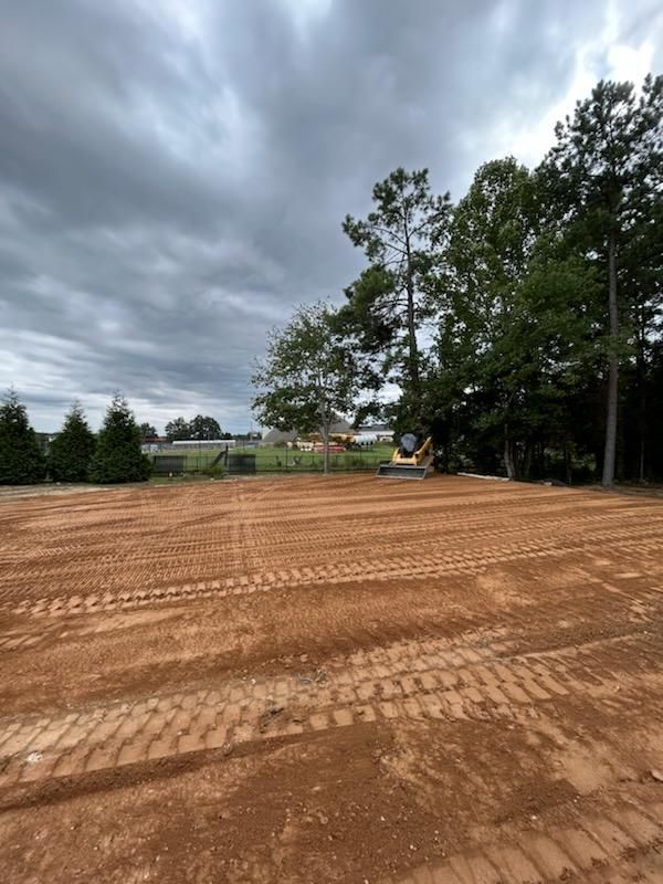 Cleared dirt lot under cloudy sky beside trees and a grassy field
