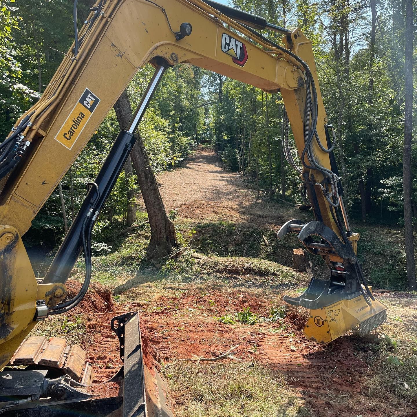 Yellow CAT excavator clearing a forest path, with trees and dirt around it.