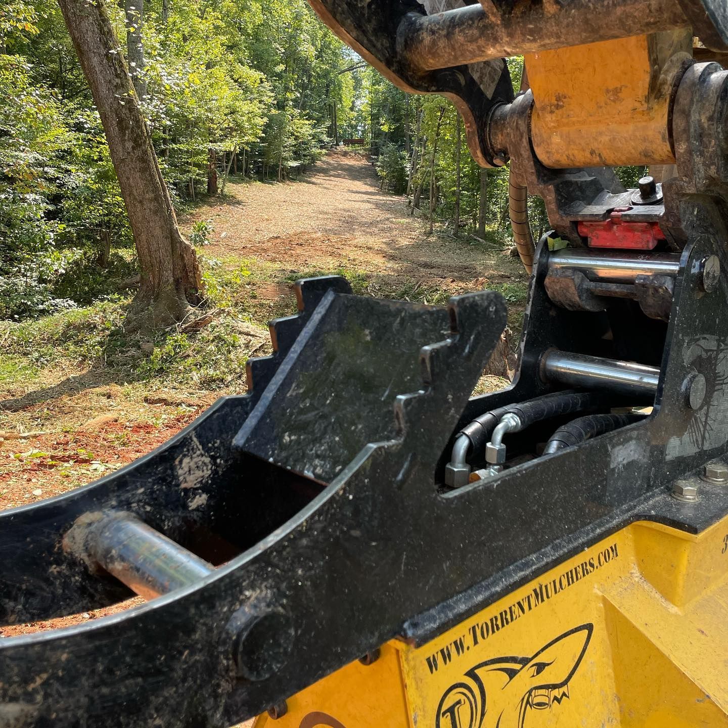 Yellow excavator bucket digging a dirt path in a wooded area