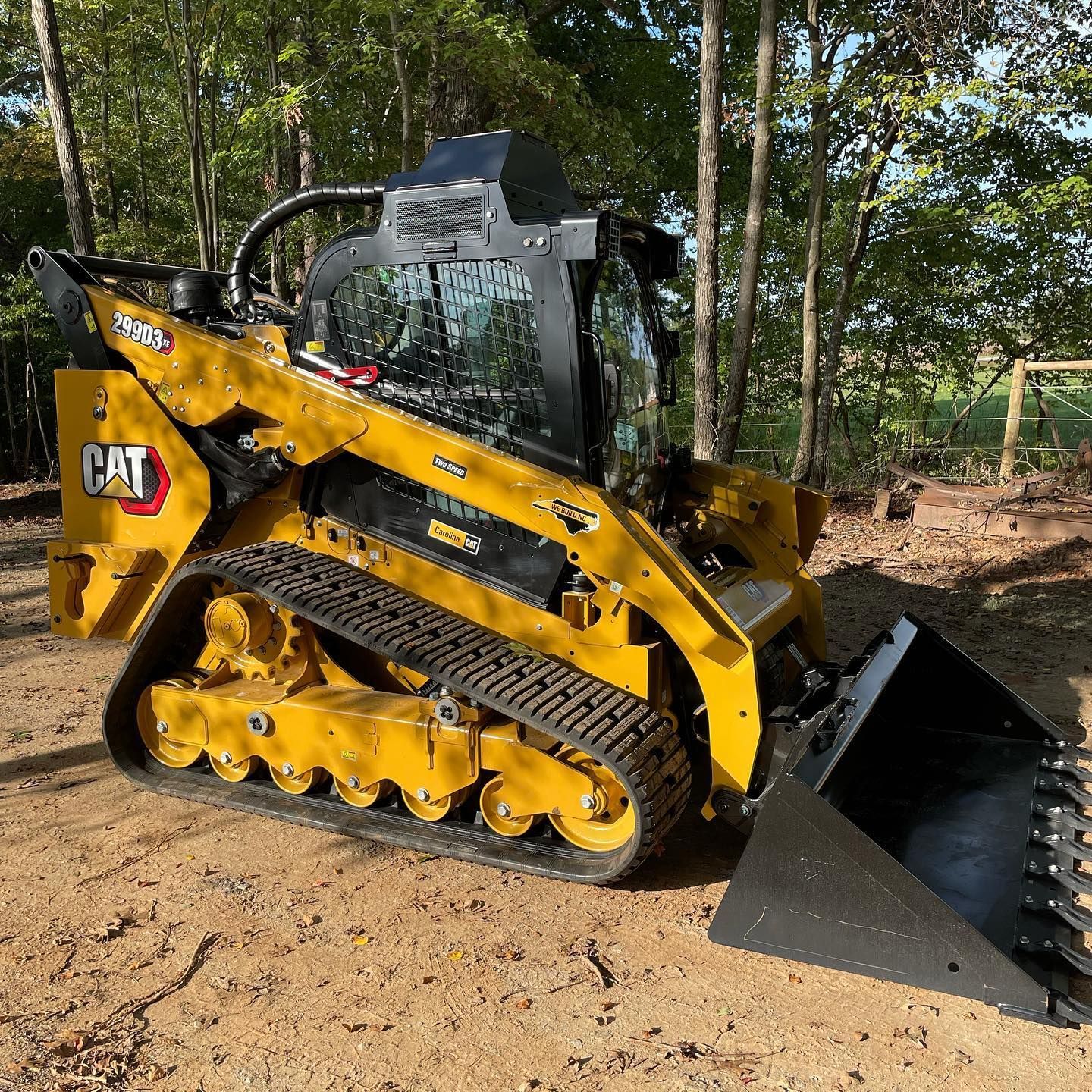 Yellow CAT skid steer with bucket in a wooded dirt area