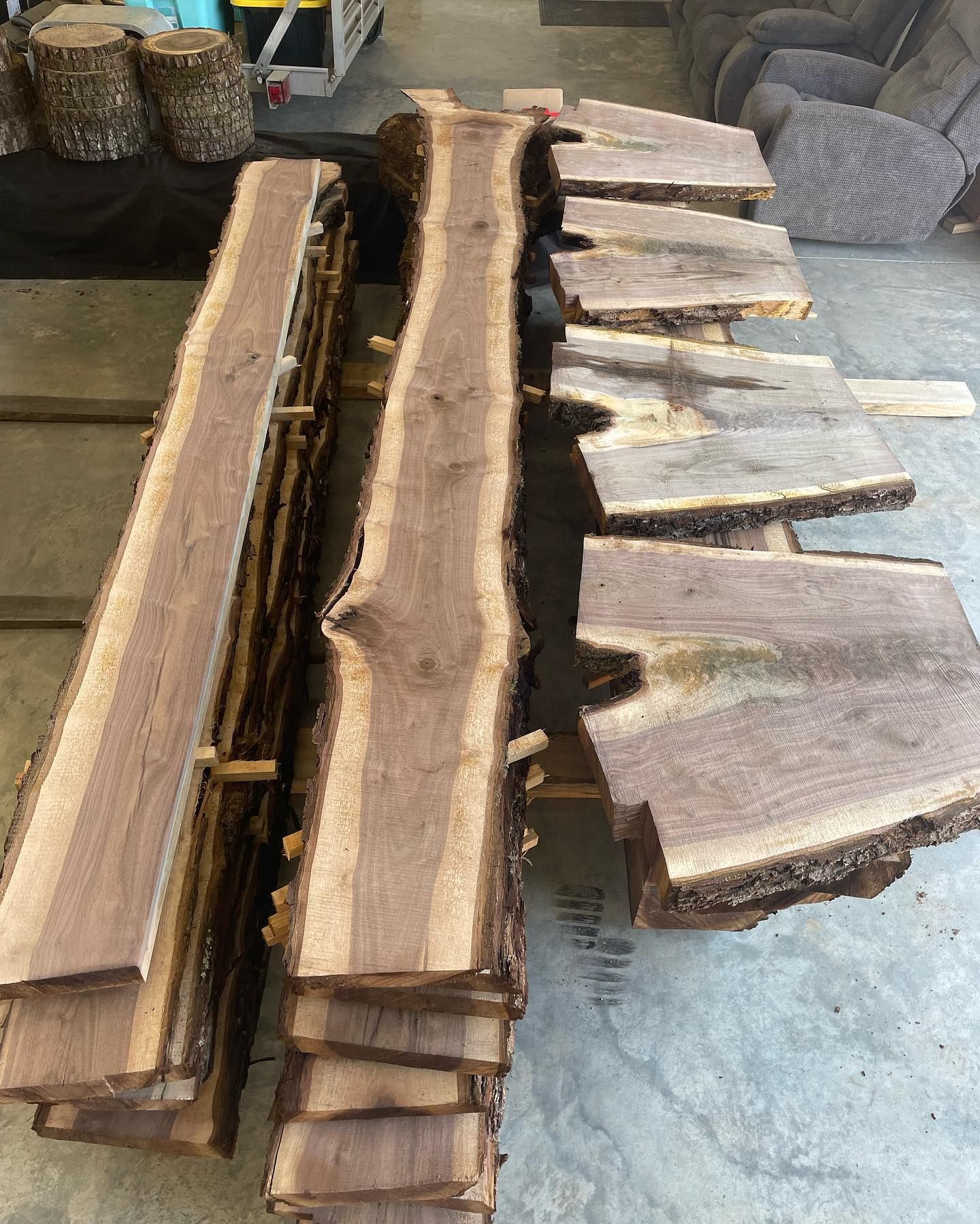 Stacked rough-cut wood slabs and planks on a gray floor in a workshop or garage.