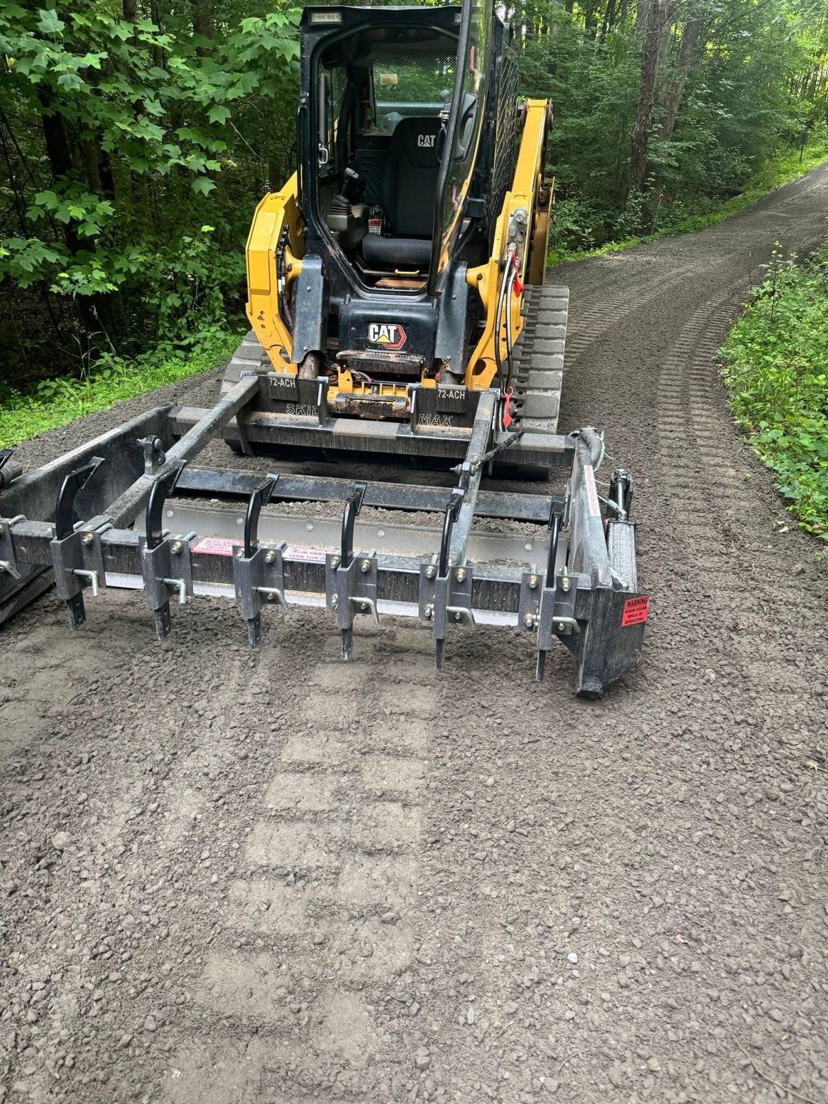 Yellow skid steer grading a gravel path beside a forest