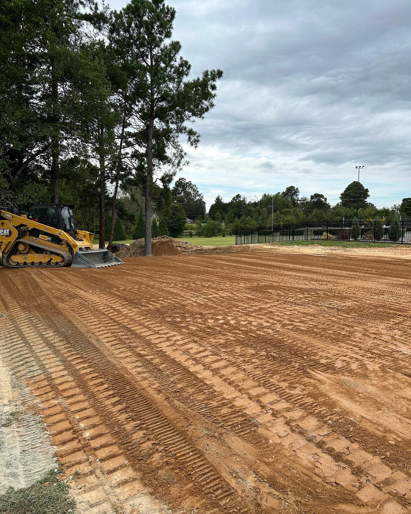 Construction site with a bulldozer grading a dirt lot beside trees under a cloudy sky