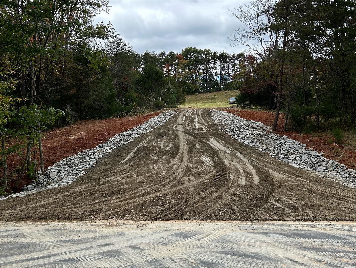 Gravel road under construction through a wooded area on an overcast day