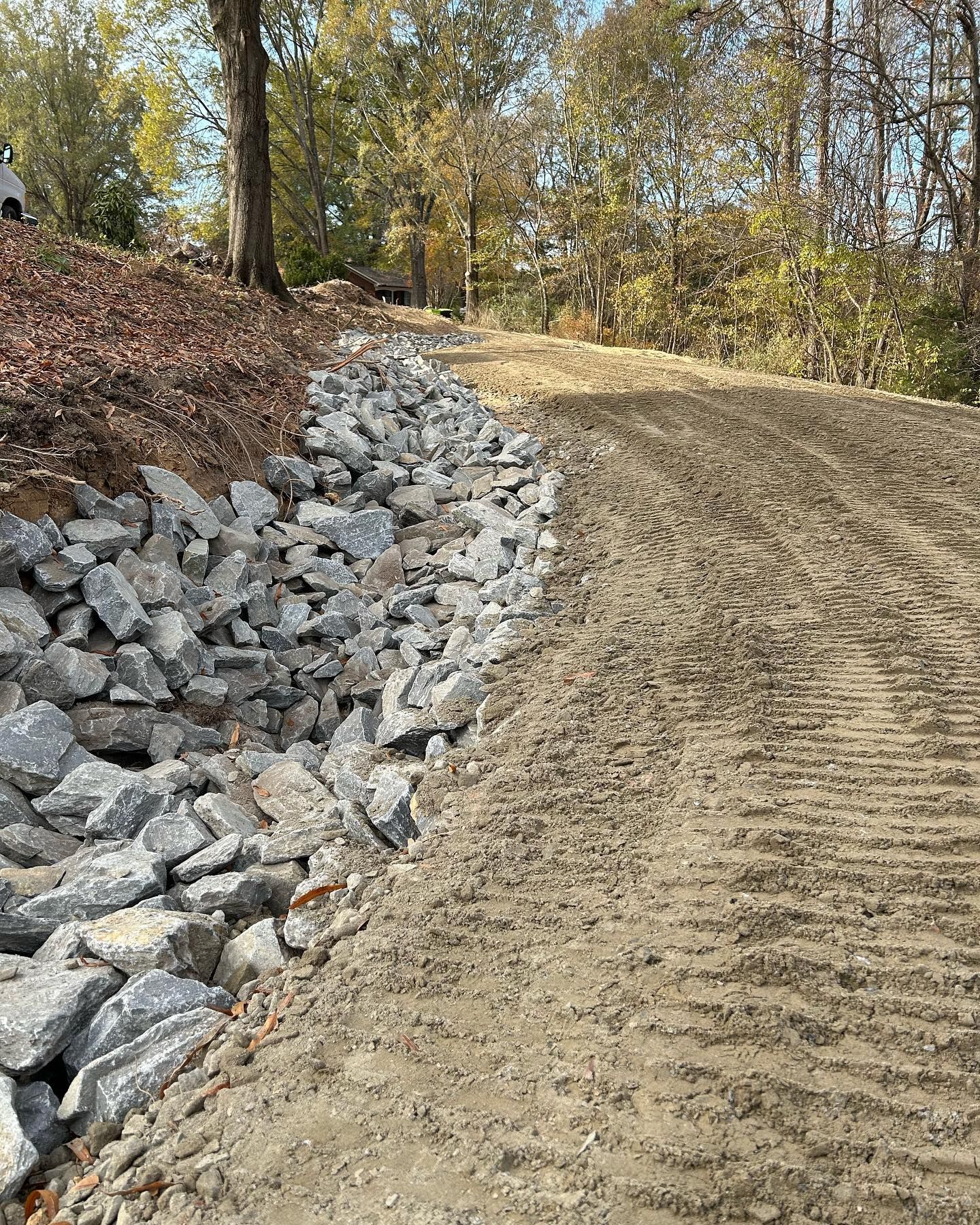 Graded dirt slope beside a rocky retaining wall in a wooded area