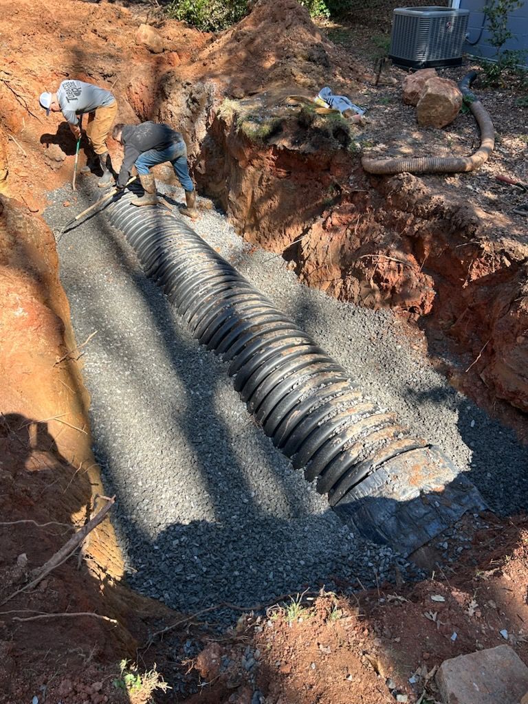Workers installing corrugated drainage pipe in a dirt trench at a construction site