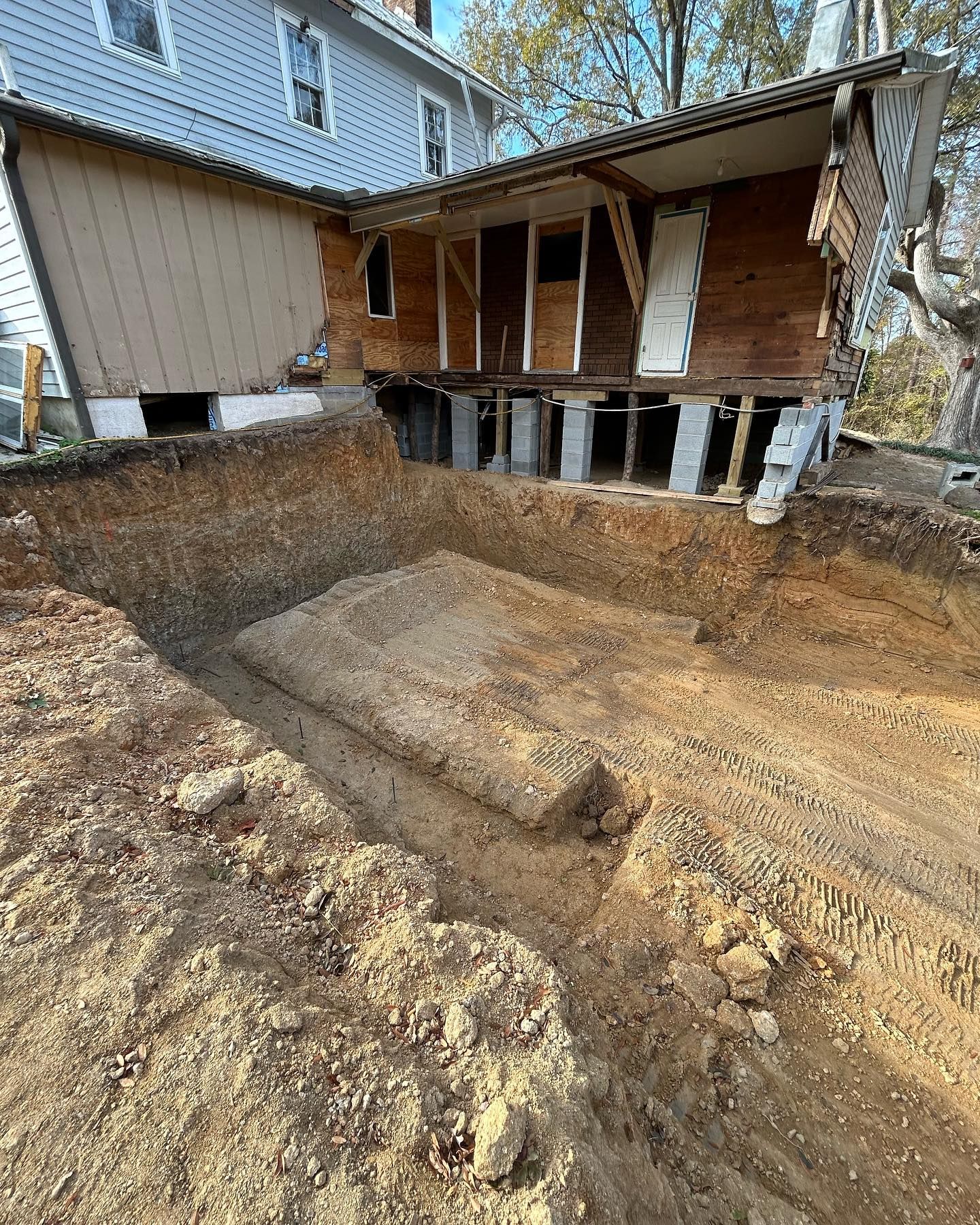House foundation excavation with a dirt pit and exposed crawlspace under a wooden porch.