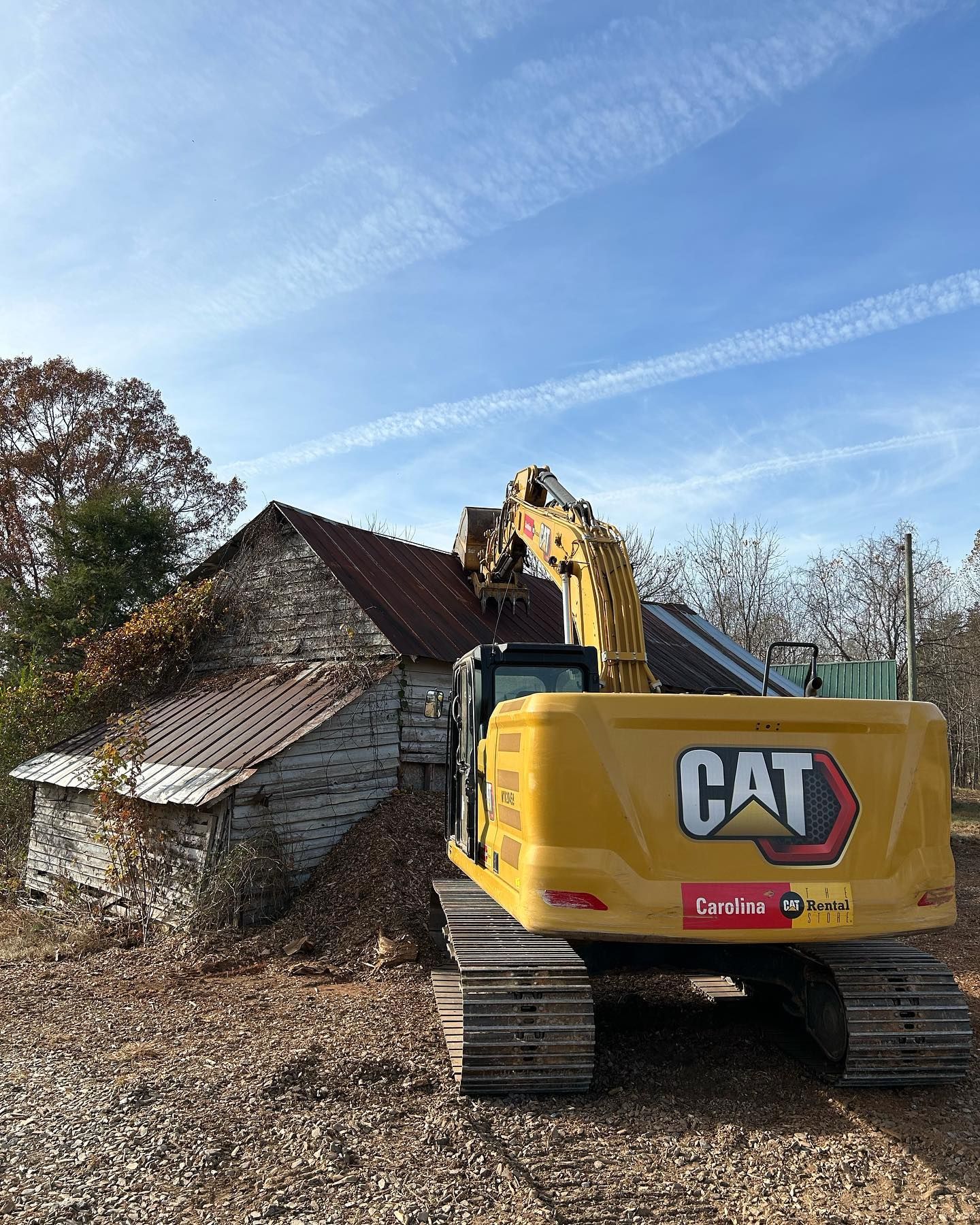 Yellow CAT excavator beside a crumbling stone building on a leaf-covered site under a blue sky