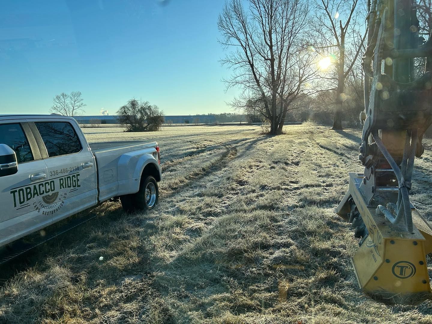Frosty field at sunrise with a white pickup truck on the left and farm equipment on the right.
