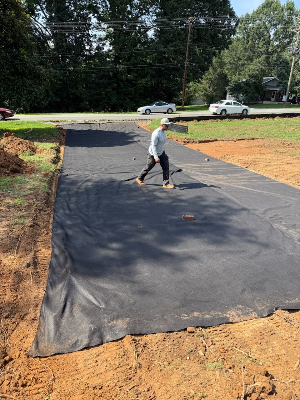 Worker spreading black landscape fabric over a driveway area outdoors