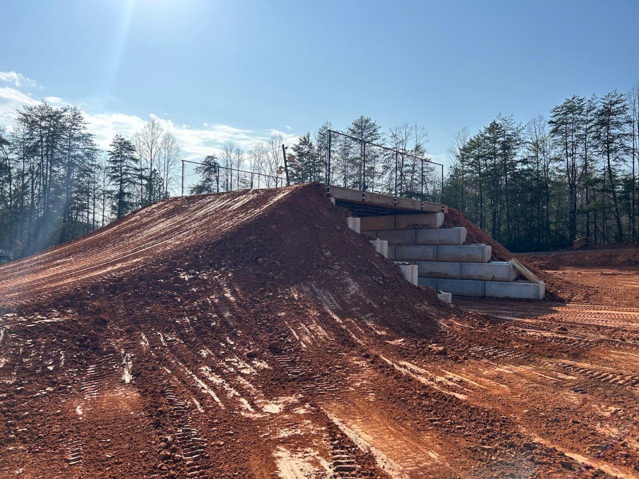 A large reddish dirt mound beside stacked concrete blocks at a construction site under a clear sky.