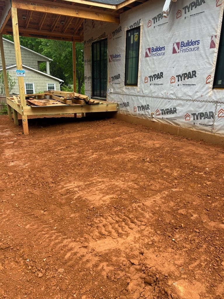 Unfinished house exterior with Typar wrap, wooden porch, and red dirt ground under construction