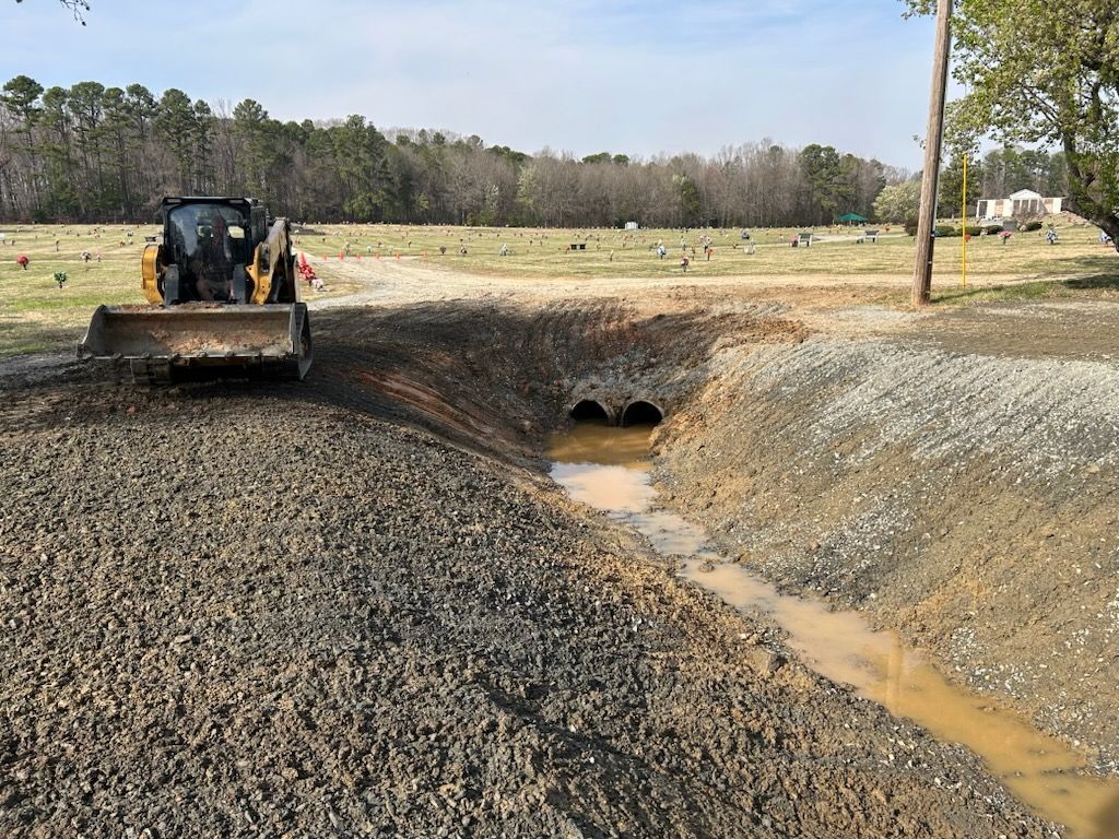 Bulldozer beside muddy drainage ditch with culvert pipes in a rural field
