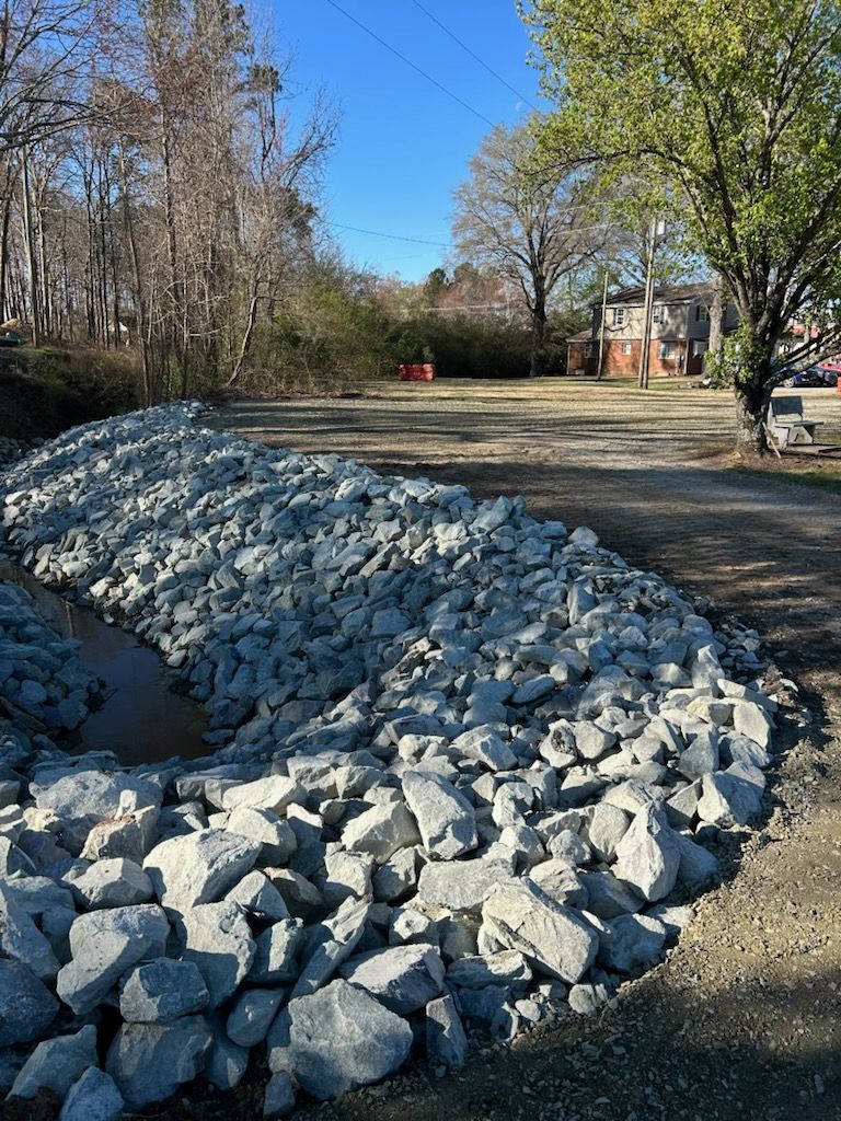 Rocks piled along a dirt road beside leafless trees under a clear blue sky