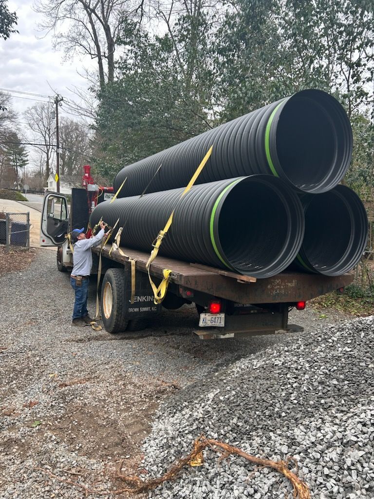 Worker loading large black drainage pipes onto a truck at a roadside construction site