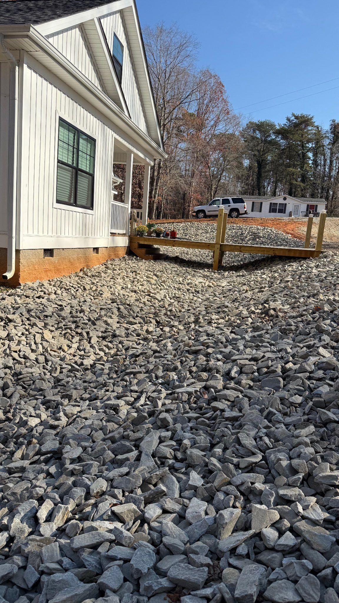 House exterior with white siding beside a gravel-covered yard and a wooden railing under a blue sky