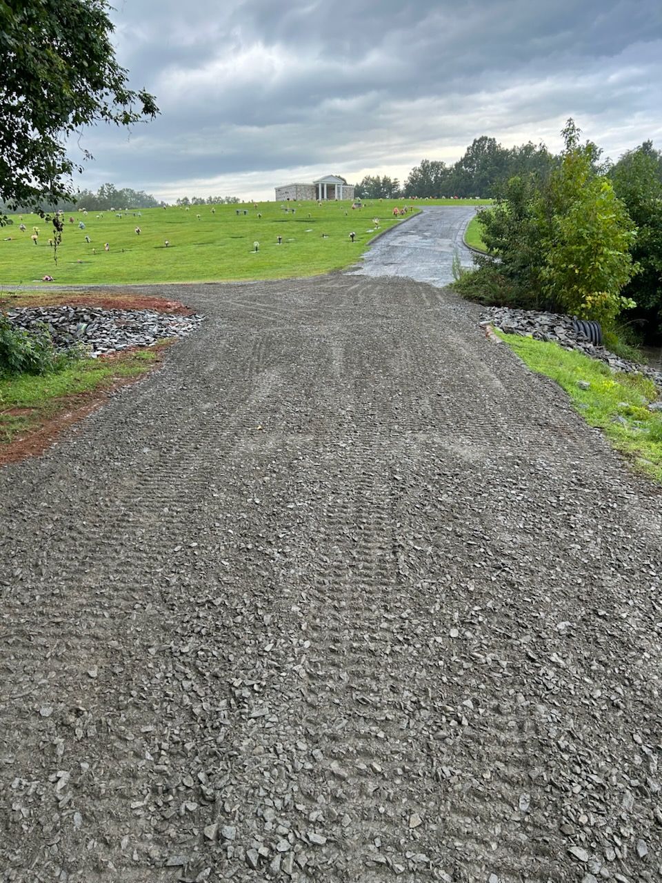 Gravel path leading through a green field under a cloudy sky after rain