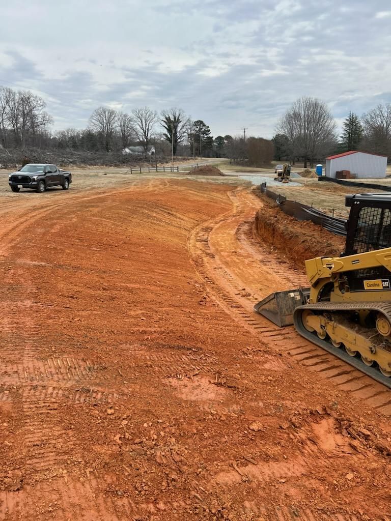 Construction site with red dirt road, bulldozer, and pickup truck under a cloudy sky