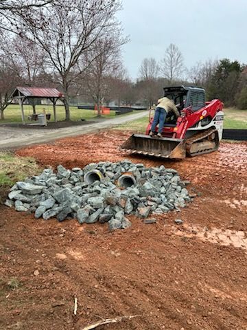Construction crew loading broken concrete into a red skid steer at a park site