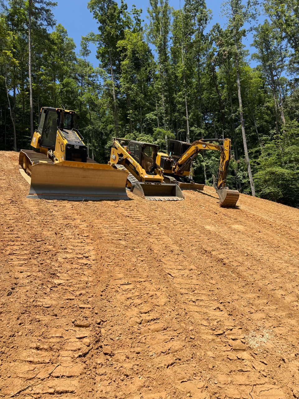 Bulldozer and excavator grading a dirt road in a wooded construction site