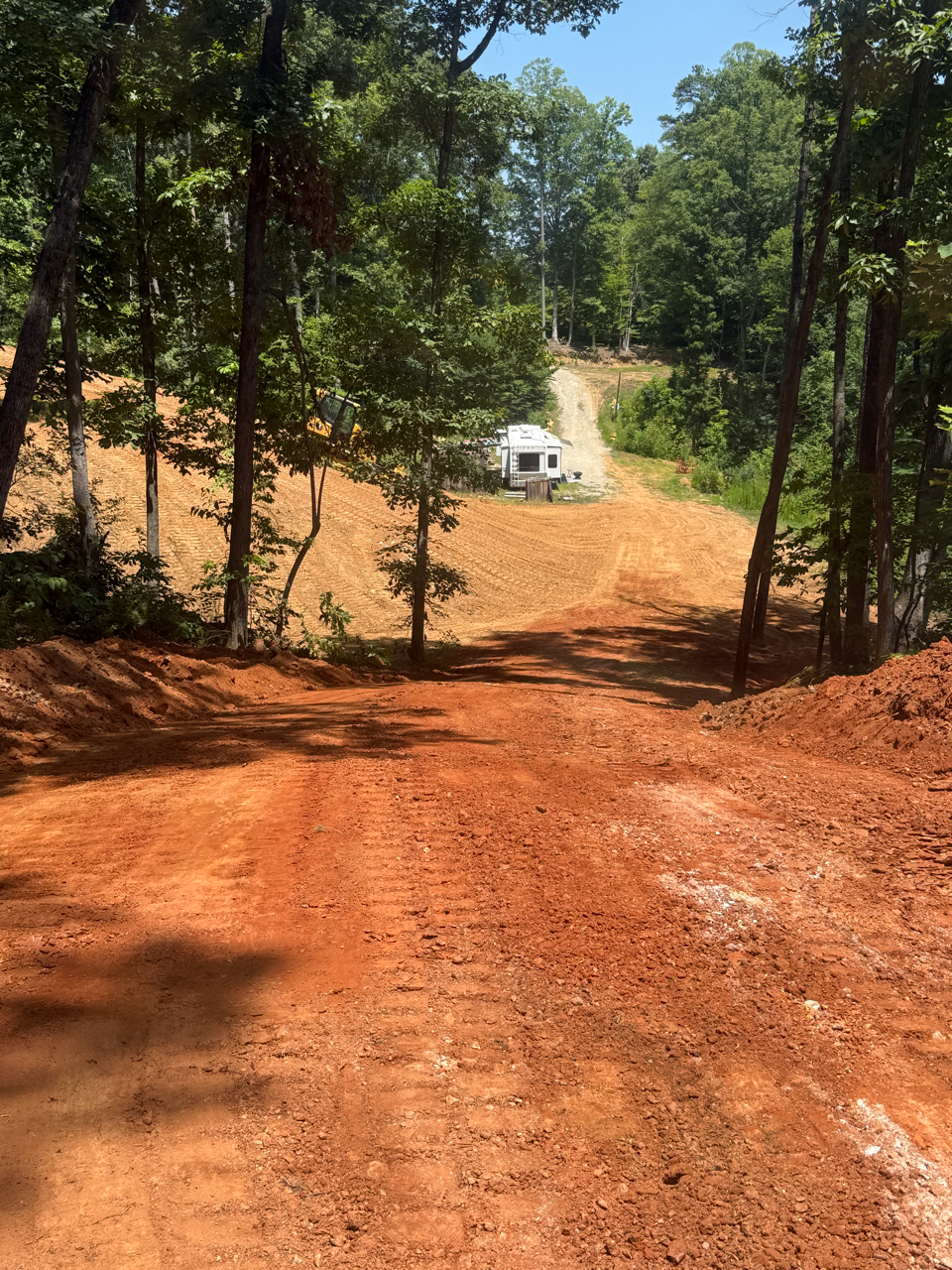 Red dirt road through tall pine trees, with a white off-road vehicle in the distance.