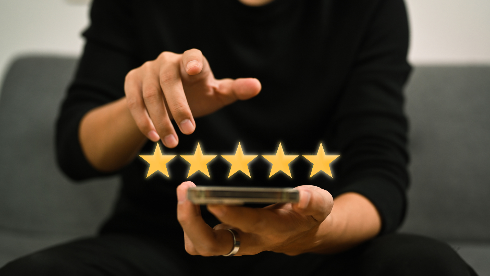 Hand tapping five-star rating above a smartphone on a gray couch