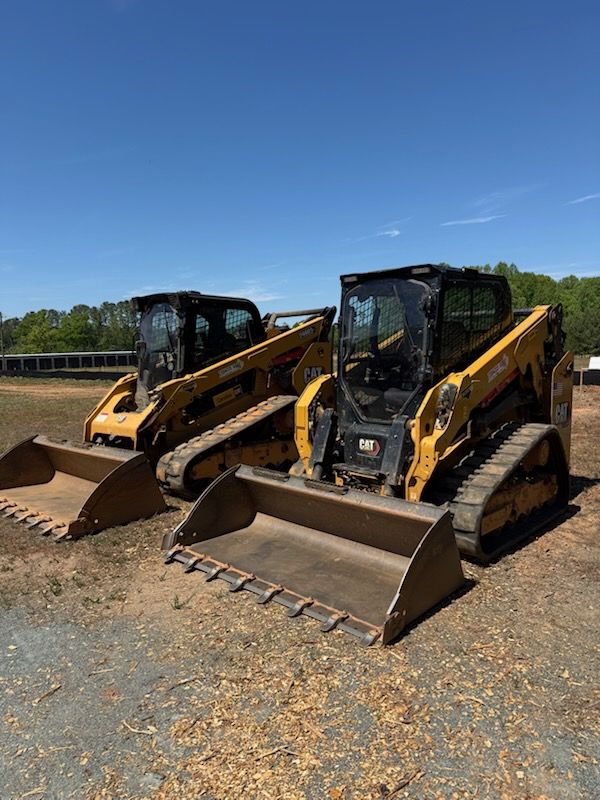 Two yellow construction loaders parked side by side on a gravel lot under a blue sky