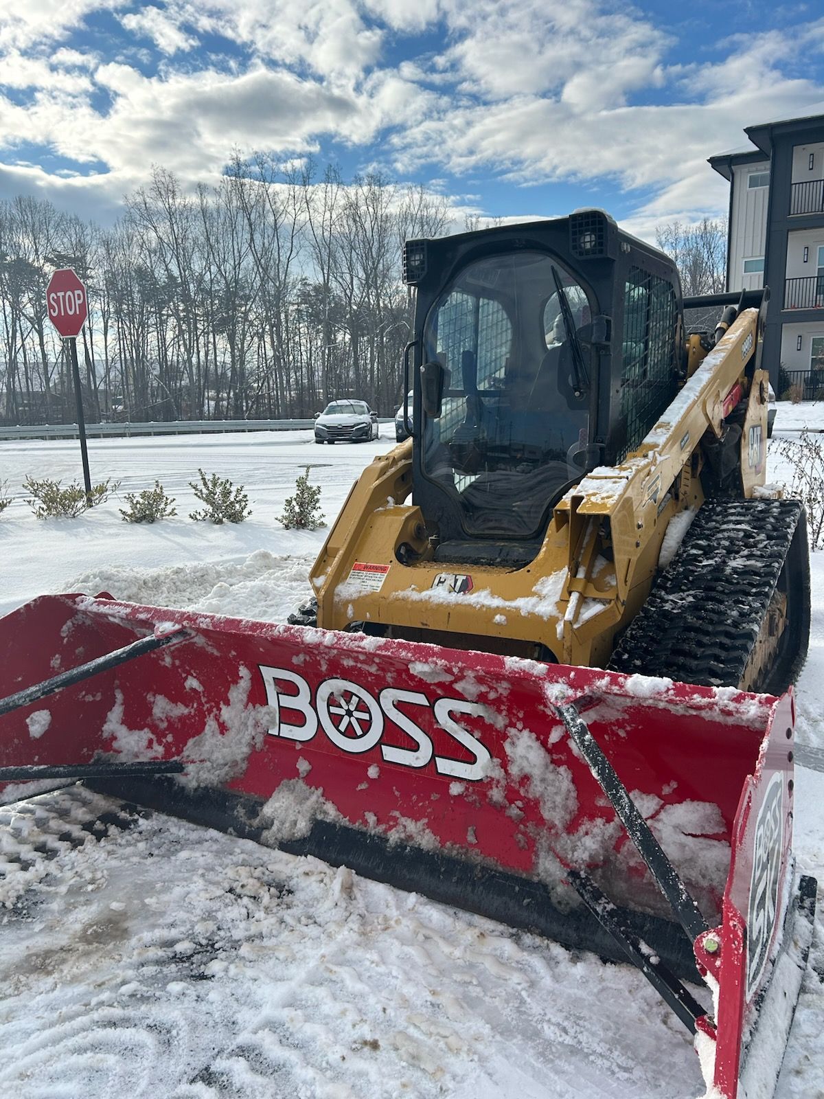 Yellow snowplow with red blade clearing snow in a snowy parking lot