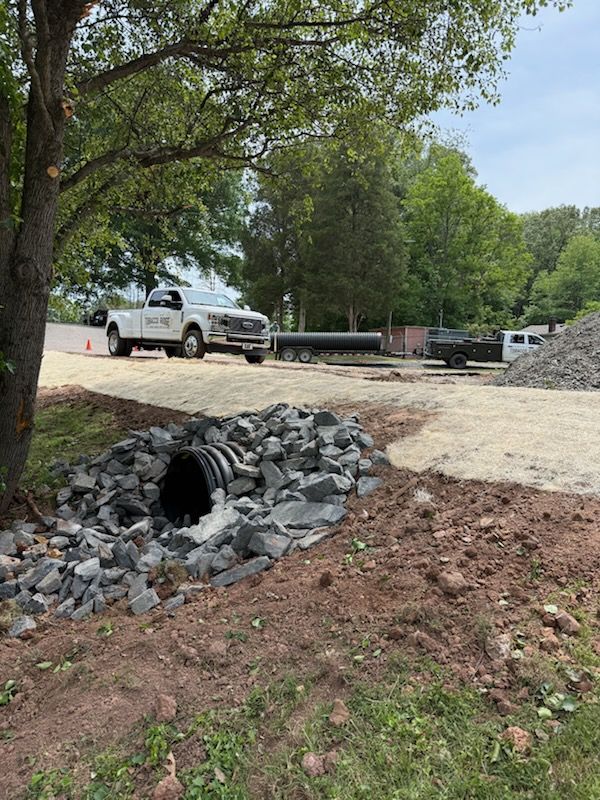 White pickup truck near a rocky drainage culvert under trees by a gravel road