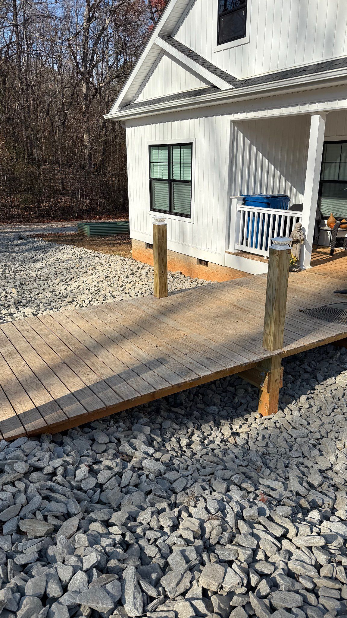 White house entrance with a wooden accessibility ramp over gravel, and a blue chair on the porch.