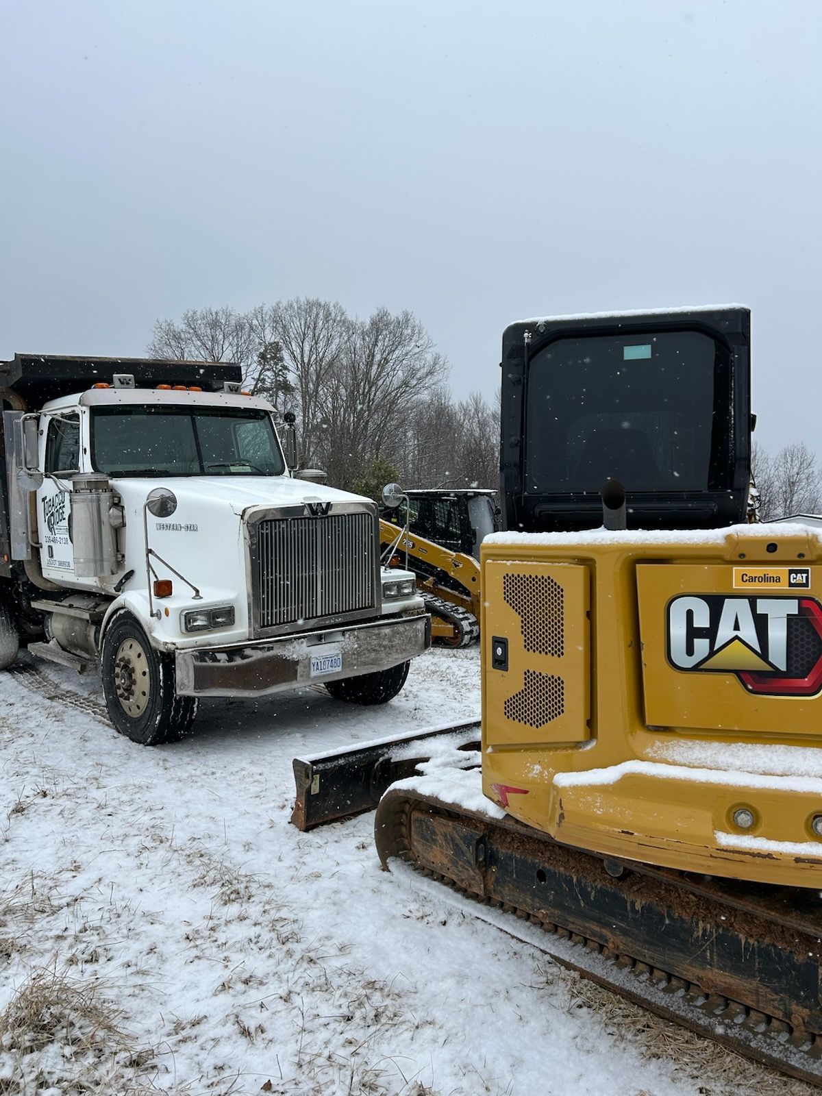 Snowy construction site with a white dump truck beside a yellow CAT bulldozer