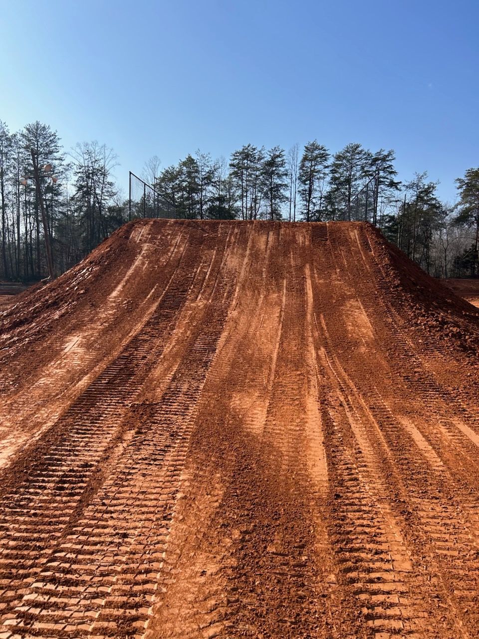 Dirt motocross jump ramp on a cleared track with trees in the background under a blue sky