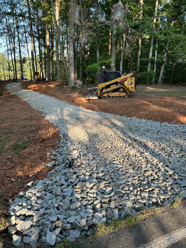 Skid steer spreading gravel on a winding path through a wooded area