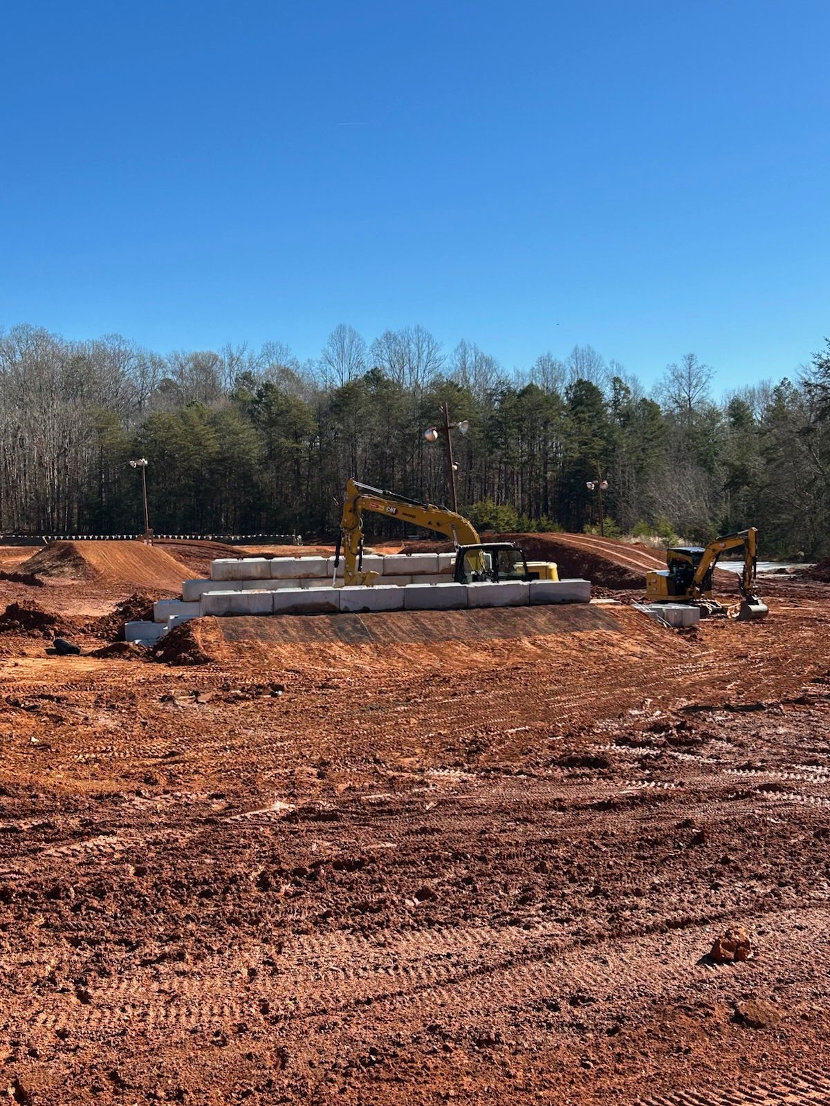 Construction site with excavator and concrete foundation in a cleared dirt field under a blue sky