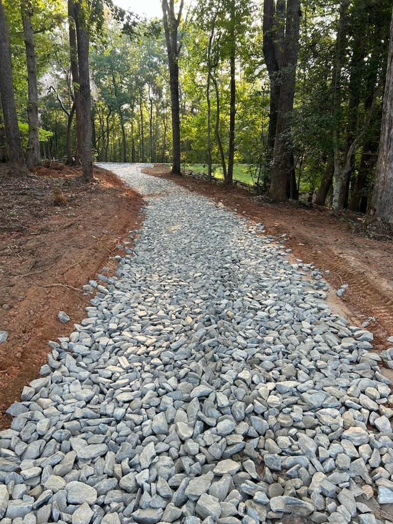 Rocky gravel trail winding through a wooded forest with tall trees and brown dirt edges