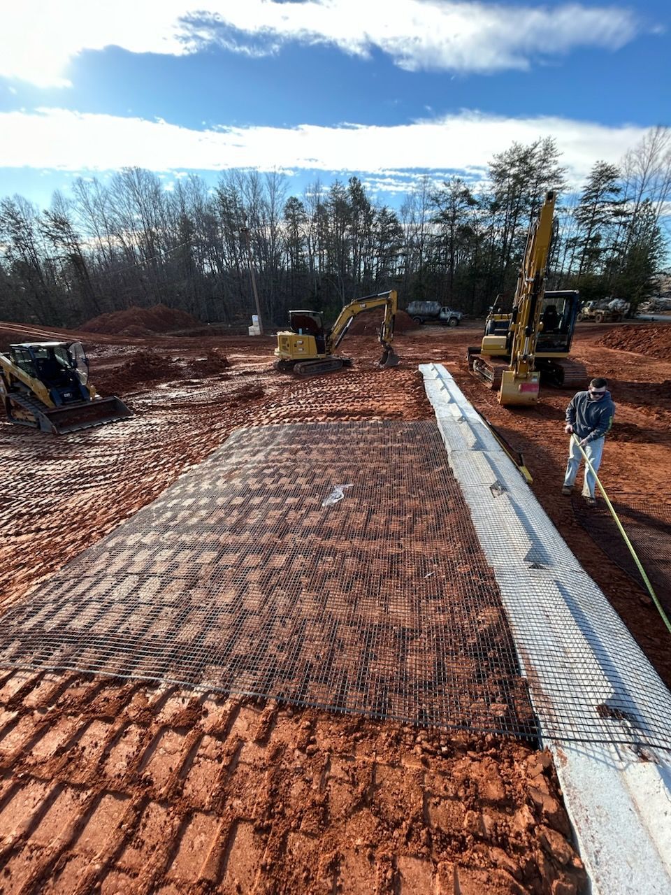 Construction site with excavators grading red soil beside a gravel path under a cloudy sky