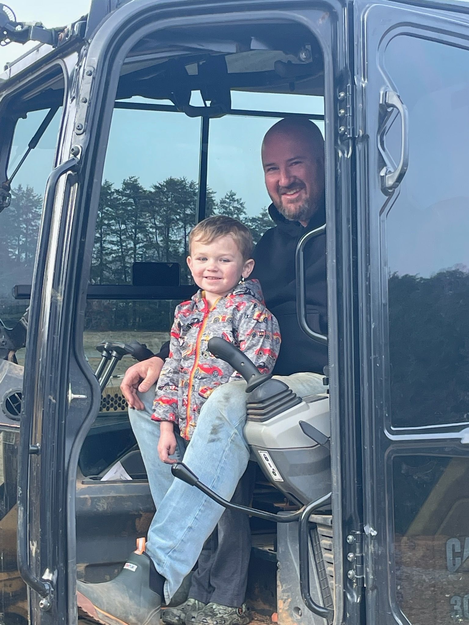 Adult and child sitting in a vehicle cab, smiling through the open door.