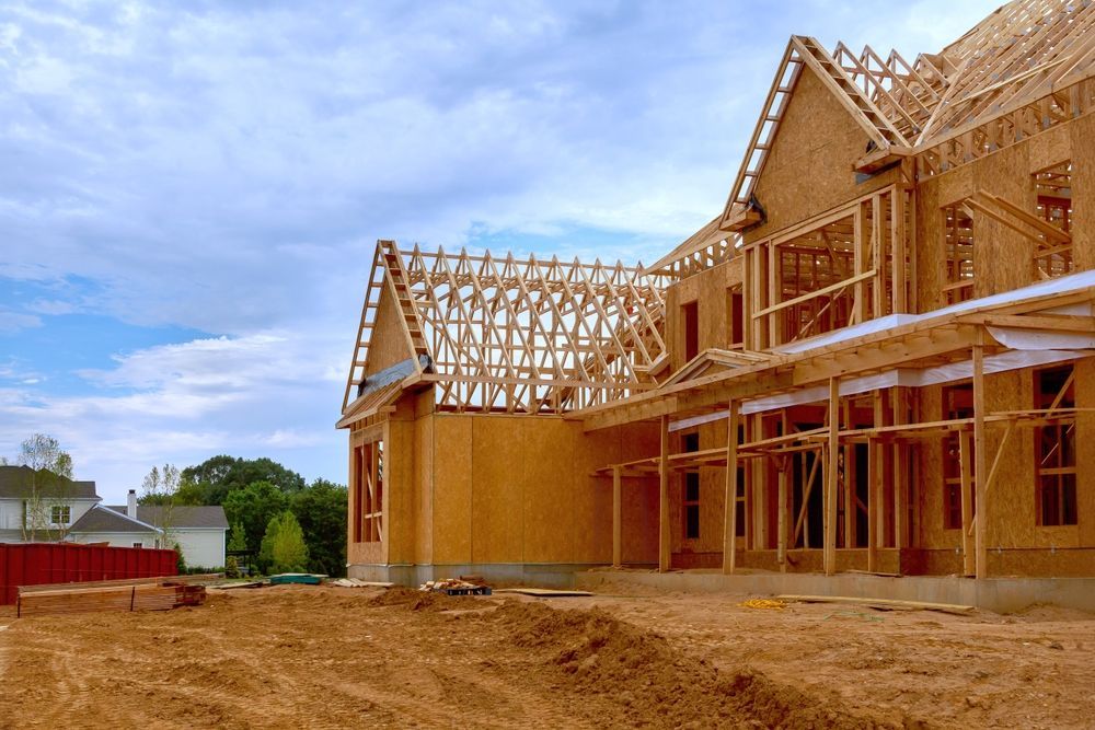 Wood-framed house under construction on a sandy lot, with a partly cloudy sky.