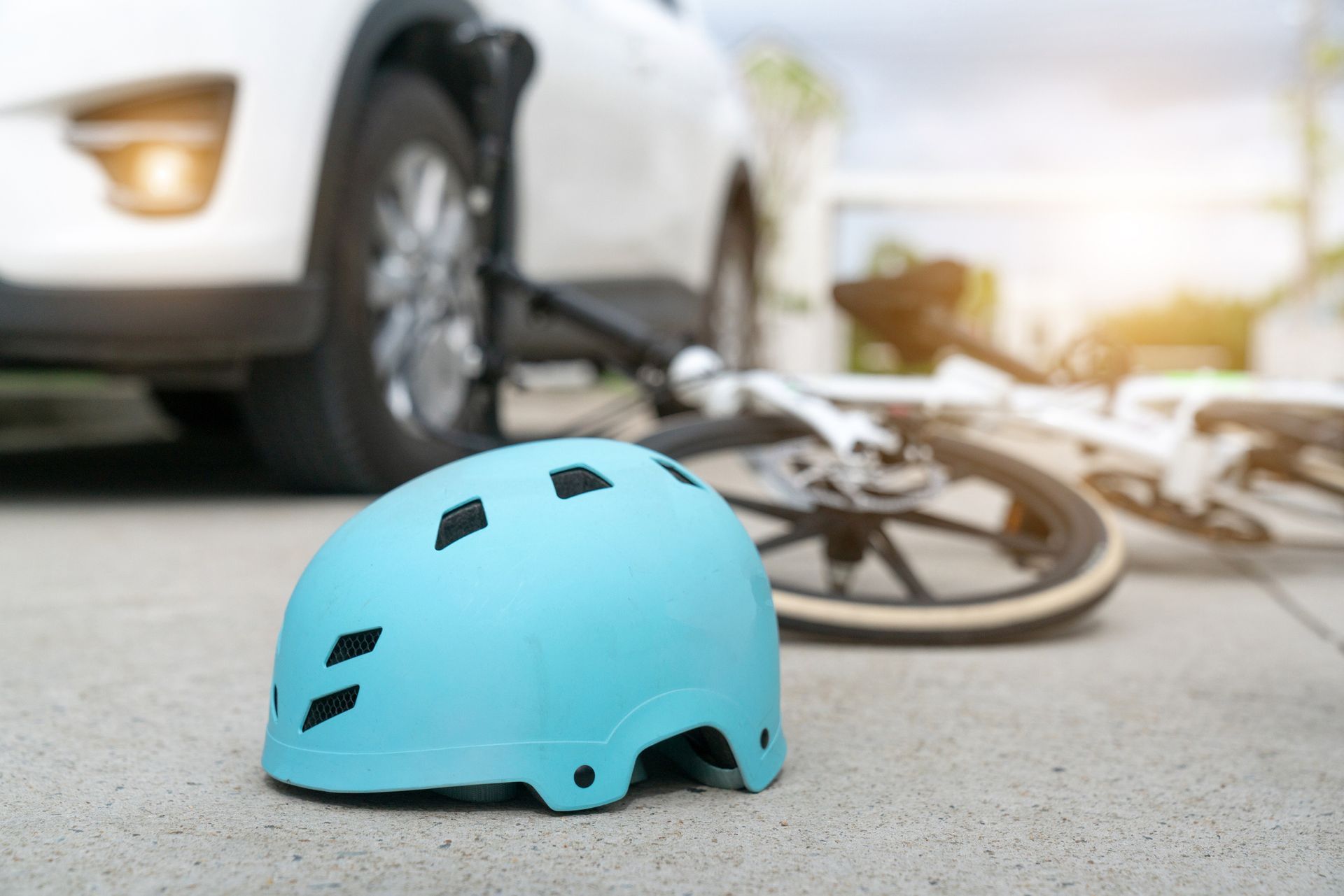 Light blue bicycle helmet on pavement, near a crashed bicycle and a white car.