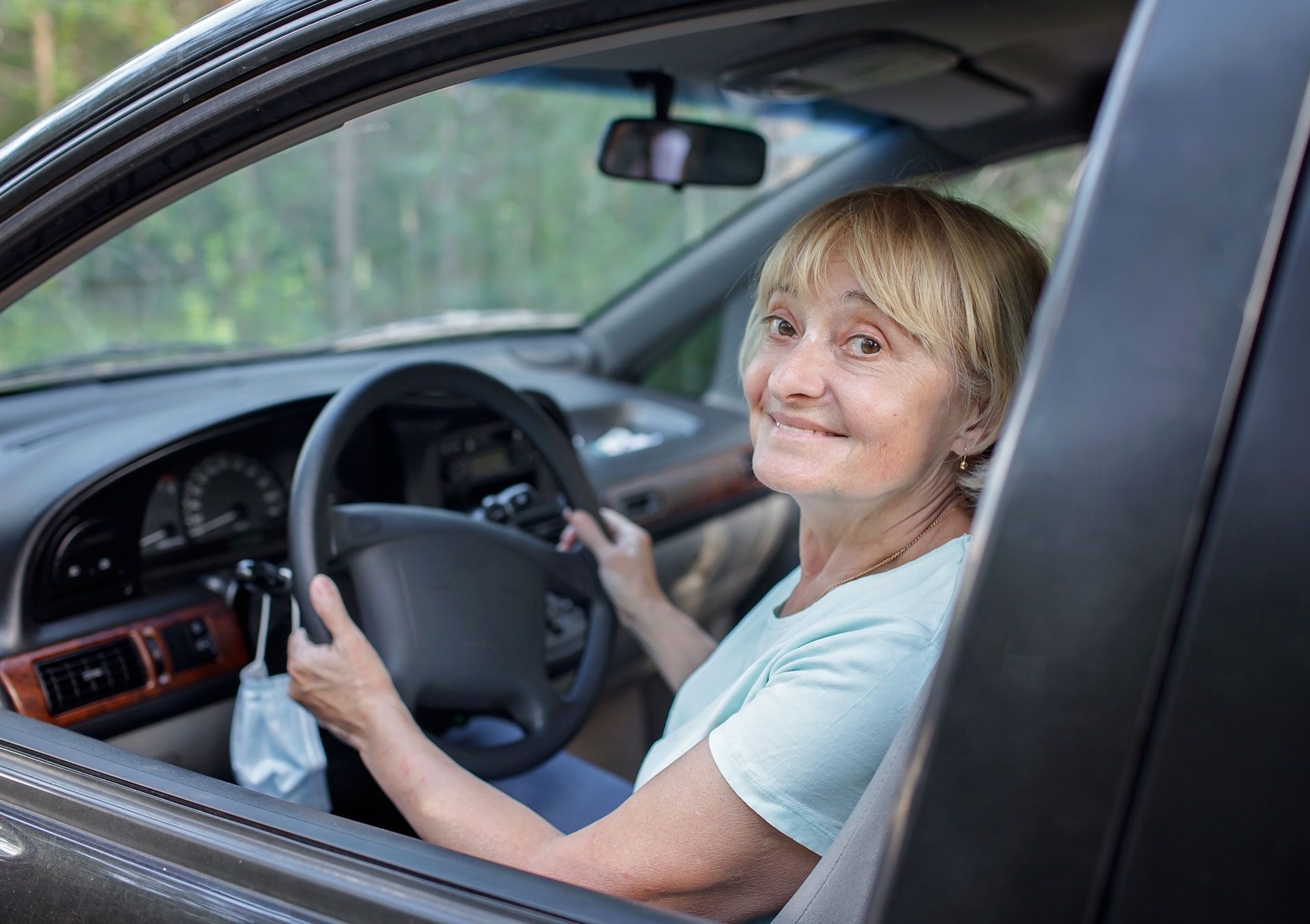 An elderly woman is sitting in the driver 's seat of a car.