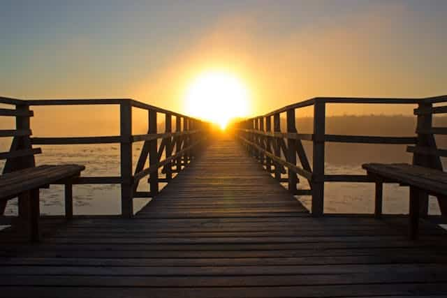 A wooden pier leading to the ocean at sunset.