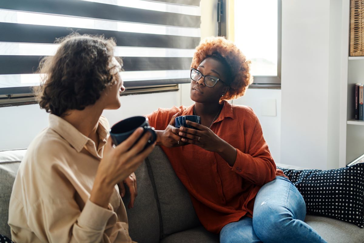 A man and a woman are sitting on a couch drinking coffee.