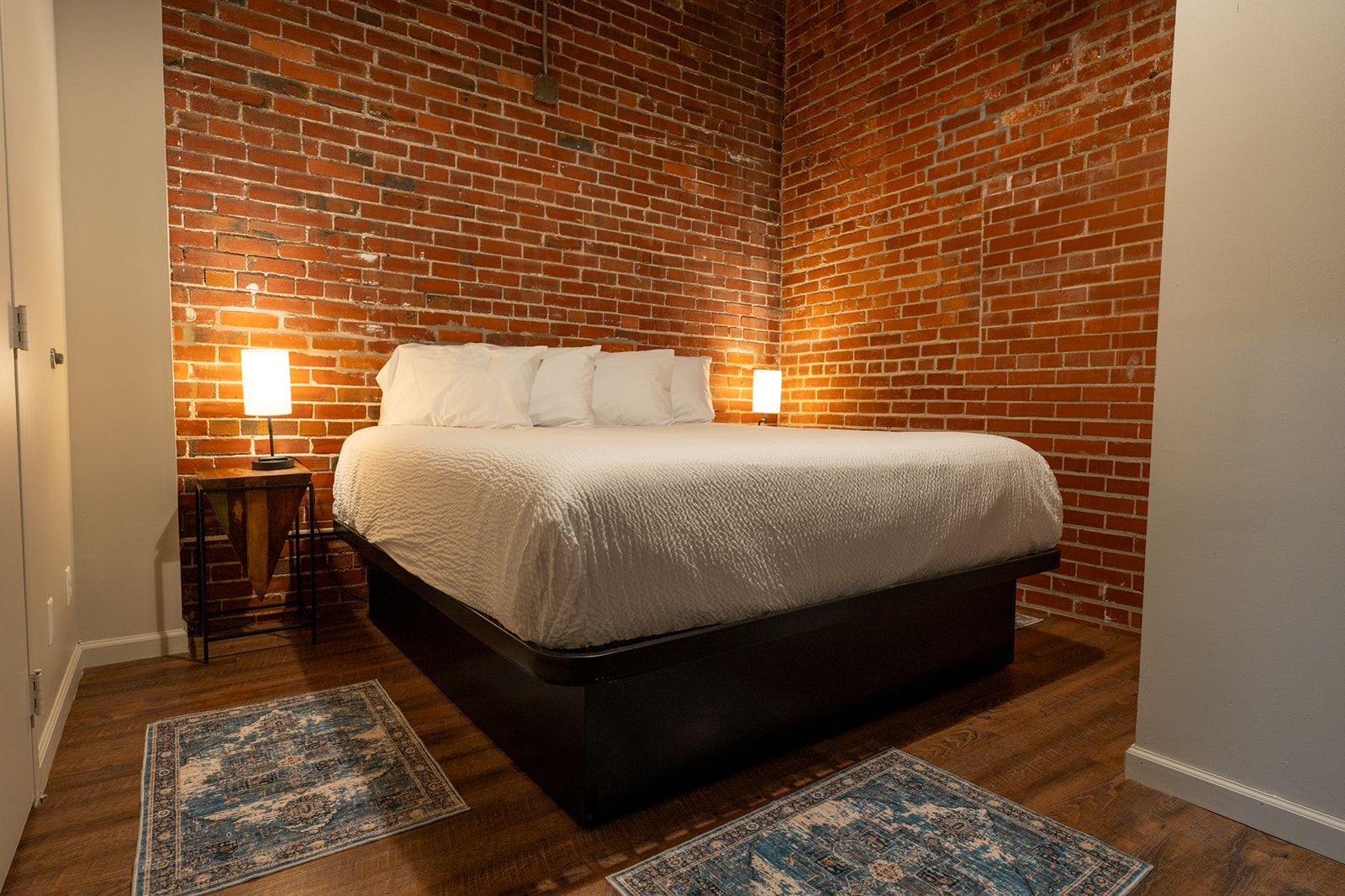 Bed in room with brick wall and industrial-style light fixture.