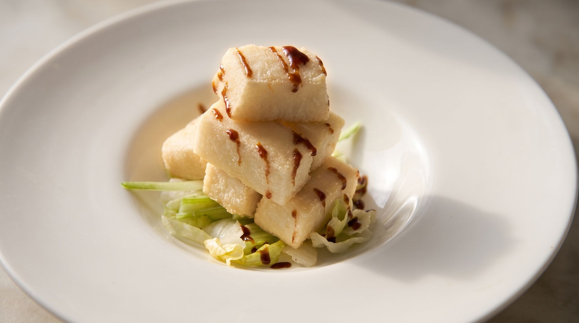 Plated scallop appetizer with seared pieces and green garnish on a white dish