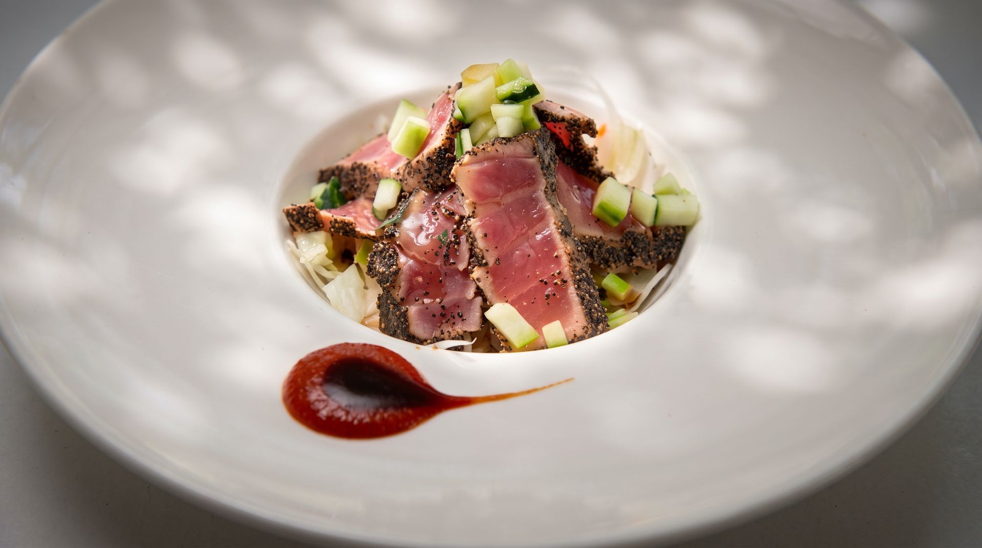 Gourmet tuna tartare with avocado and herbs in a white bowl, accented by a red sauce drizzle.
