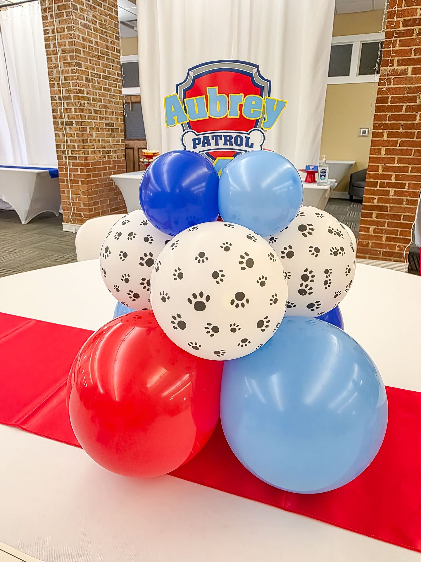 Paw Patrol balloon centerpiece with red, blue, and paw print balloons on a red table runner.